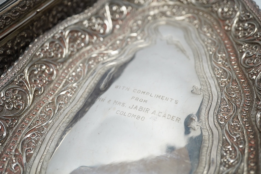 A Thai white metal cigarette box, wood lined, stamped Thainakon, 20cm and a Ceylonese white metal dish, shaped in the form of the country, with embossed borders, and inscription, maker’s mark SS, 24.7cm long, 182g. Condi